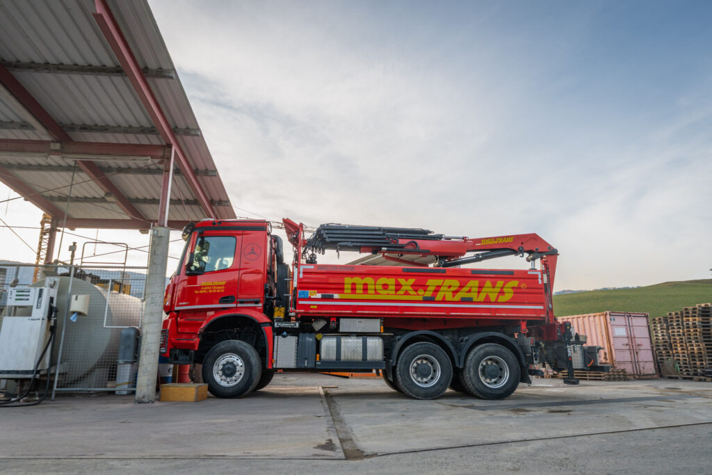 Sie sehen einen 3 Achs Kipper mit Kran und Allrad. Flexible und zuverlässige Transportlösungen für Schüttgut, Asphalt sowie voluminöse und pulverförmige Güter inklusive Hebearbeiten – effizient und verlässlich umgesetzt durch einen modernen Fuhrpark und qualifizierte Fahrer.