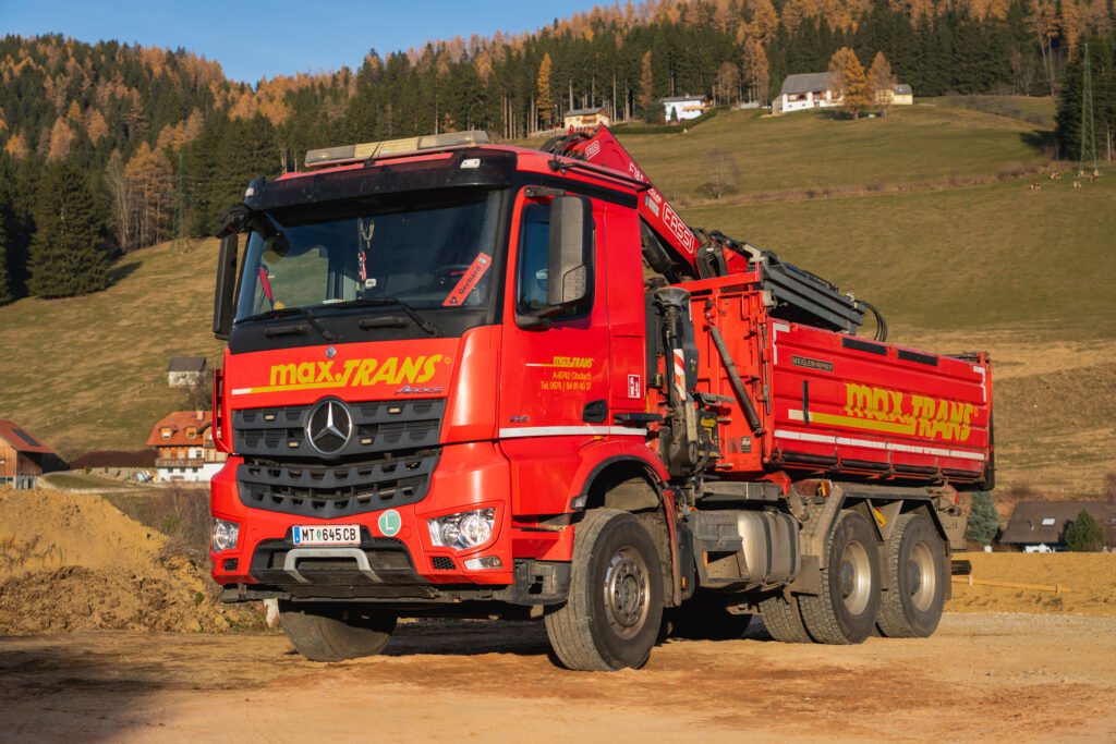 Sie sehen einen 3 Achs Kipper mit Frontkran von maxTRANS. Flexible und zuverlässige Transportlösungen für Schüttgut, Asphalt sowie voluminöse und pulverförmige Güter inklusive Hebearbeiten – effizient und verlässlich umgesetzt durch einen modernen Fuhrpark und qualifizierte Fahrer.